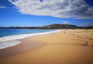 Persona caminando sola por una playa desierta cerca de Résidence U Livanti Belvédère Campomoro, Francia, con colinas al fondo.
