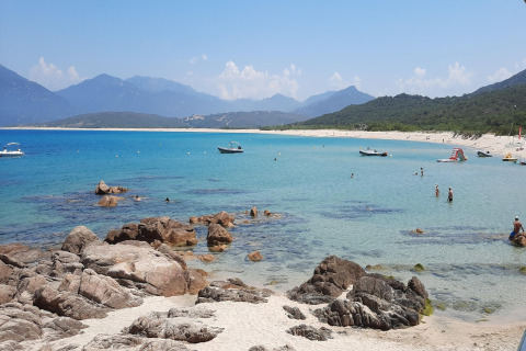 Impresionante playa de arena y mar azul desde Résidence U Livanti Belvédère Campomoro, Francia, con personas y botes.