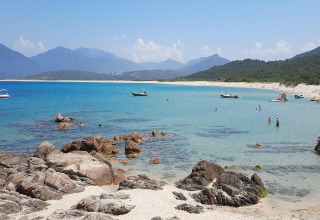 Impresionante playa de arena y mar azul desde Résidence U Livanti Belvédère Campomoro, Francia, con personas y botes.