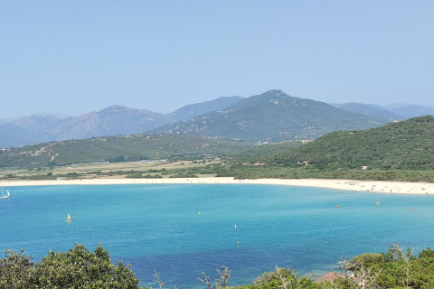Vista del mar turquesa, playa de arena y montañas verdes desde Résidence U Livanti Belvédère Campomoro, Francia.