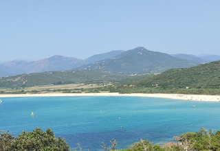 Vista del mar turquesa, playa de arena y montañas verdes desde Résidence U Livanti Belvédère Campomoro, Francia.