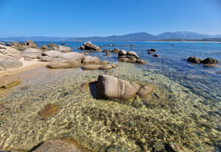 Agua cristalina y rocas en la playa del chalet Résidence U Livanti Belvédère Campomoro, Francia, con montañas.