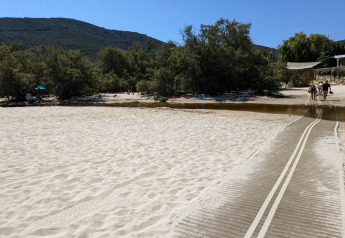 Ein Sandstrand mit Weg und kleinen Bäumen bei Résidence U Livanti Belvédère Campomoro in Frankreich.