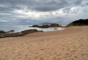 Strand mit Felsen und Sand unter bewölktem Himmel bei Résidence U Livanti Belvédère Campomoro, Frankreich.
