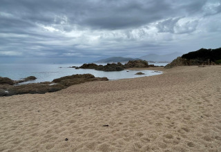 Playa de arena y rocas con cielo nublado en Résidence U Livanti Belvédère Campomoro, Francia.