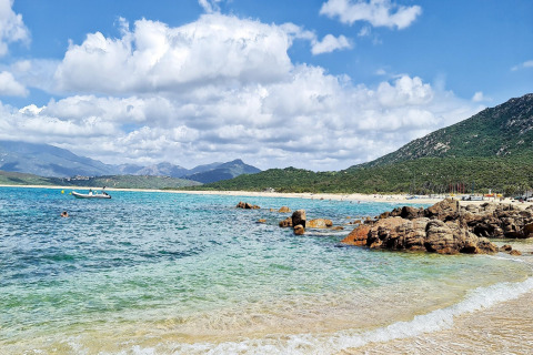Vista de playa con agua cristalina, rocas y montañas en Résidence U Livanti Belvédère Campomoro, Francia.