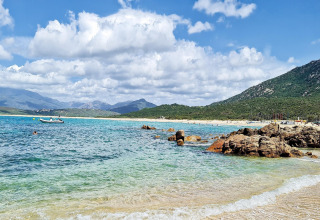 Vista de playa con agua cristalina, rocas y montañas en Résidence U Livanti Belvédère Campomoro, Francia.
