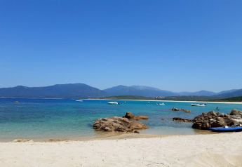 Sandstrand mit Felsen, türkisfarbenem Wasser und Booten bei Résidence U Livanti Belvédère Campomoro, Frankreich.