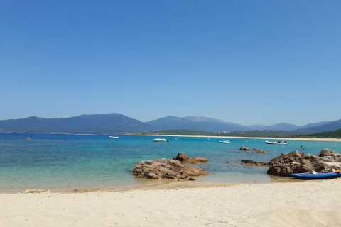 Playa de arena con rocas, agua turquesa y botes en Résidence U Livanti Belvédère Campomoro, Francia.