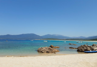 Playa de arena con rocas, agua turquesa y botes en Résidence U Livanti Belvédère Campomoro, Francia.