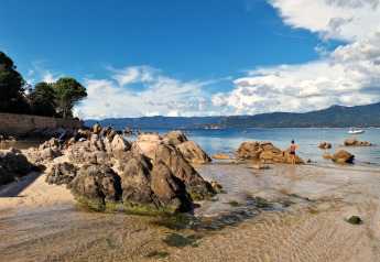 Strand mit Felsen bei Résidence U Livanti Belvédère Campomoro in Frankreich, mit Bergen im Hintergrund.