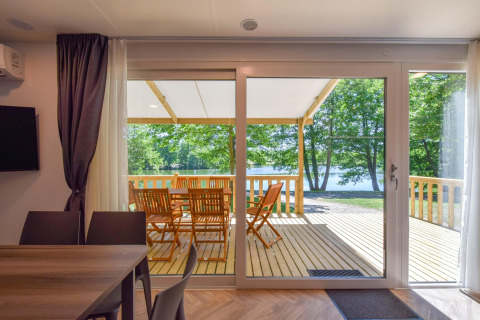 Udsigt fra stuen i mobilhome Cottage «6p» i Frankrig, med terrasse, havemøbler og sø i baggrunden.