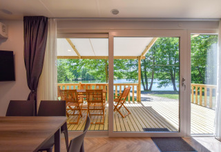 Udsigt fra stuen i mobilhome Cottage «6p» i Frankrig, med terrasse, havemøbler og sø i baggrunden.