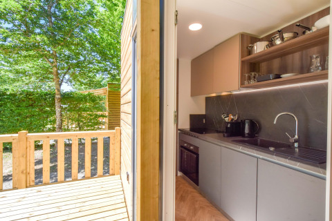 Keuken en houten terras in het mobilhome Cottage «6p» in Frankrijk met zicht op een groene tuin.