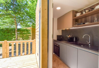 Cocina y terraza de madera en la casa móvil Cottage «6p» en Francia con vistas a un jardín verde.