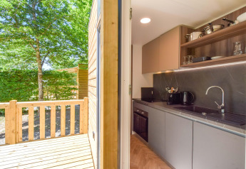 Küche und Holzterrasse im Mobilheim Cottage «6p» in Frankreich mit Blick auf einen Garten.
