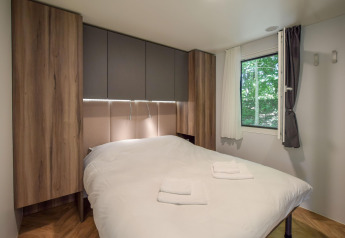 Dormitorio en la casa móvil Cottage «6p» en Francia, cama doble, armarios de madera y ventana con vista verde.