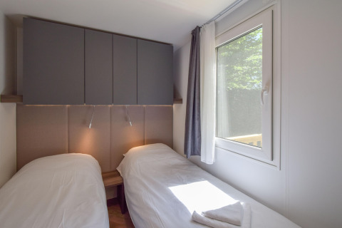 Dormitorio en la casa móvil Cottage «6p» en Francia con dos camas individuales, armarios y ventana.
