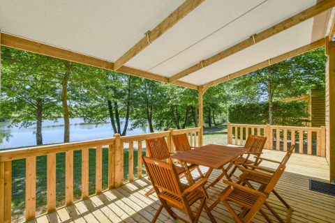 Terraza de madera con mesa y sillas en la mobil home Cottage 6p en Francia, vista al lago y árboles.