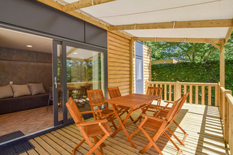 Træterrasse med seks stole og bord ved Cottage «6p» mobilhome i Frankrig, med udsigt til grønne omgivelser.