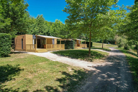 Mobilhjem Cottage '6p' i Frankrig omgivet af grønne træer, solskin og en grussti foran.