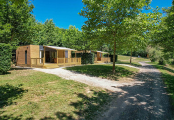 Casa móvil Cottage '6p' en Francia rodeada de árboles, césped verde y una senda soleada al frente.