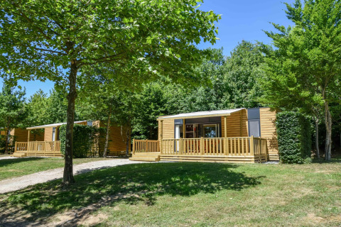 Casa móvil moderna Cottage «6p» en Francia, rodeada de árboles verdes y césped bajo cielo azul.