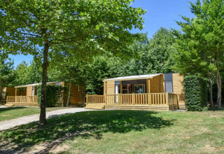 Moderne mobilhome Cottage «6p» i Frankrig, omgivet af grønne træer og græs under blå himmel.