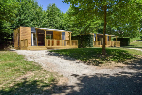 Moderne mobilhome Cottage «6p» in Frankrijk met houten terras, grasveld en omgevende bomen en zon.