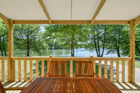 Udsigt fra træterrasse med borde og stole mod sø og grønne træer ved mobilhome Cottage 6p i Frankrig.