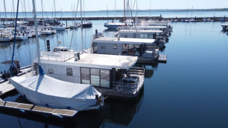 Houseboats docked in a marina alongside sailboats on calm, clear water under a blue sky.
