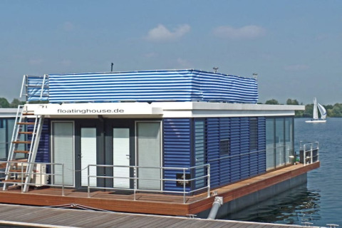 Modern huisboot met blauwe en witte strepen, terras en daktoegang, drijvend op een mooi meer.