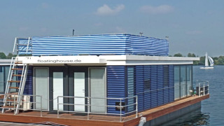 Moderne huisboot met blauwe en witte strepen, terras en daktoegang, drijvend op een prachtig meer.