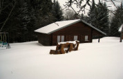 Verschneites Holzchalet 'Ronds Chetys' in Frankreich, umgeben von Tannen, ruhige Winterlandschaft.