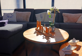 Wohnbereich im Hausboot mit grauem Sofa, Kissen, Holztisch, Orchidee und maritimer Dekoration.
