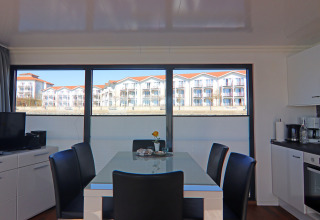 Dining area on a houseboat, featuring large windows with a view of white buildings with red roofs.