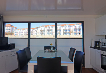 Sala da pranzo su una casa galleggiante con ampie finestre e vista su edifici bianchi dai tetti rossi.