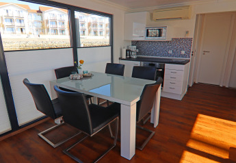 Interno di houseboat moderno con tavolo da pranzo, sei sedie nere, angolo cottura e ampie finestre sull'acqua.