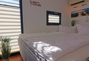 Camera da letto su una houseboat con letto matrimoniale, grandi finestre, pianta e decorazione marina.