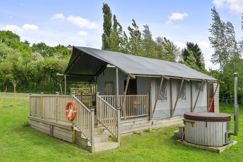 The Herdwick Safari Tent met houten veranda en hottub, gelegen in een groen veld omringd door bomen.