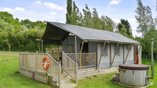 The Herdwick Safari Tent met houten veranda en hottub, gelegen in een groen veld omringd door bomen.