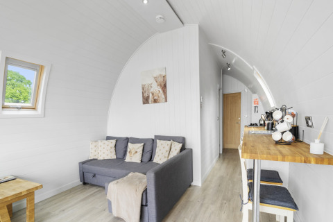 Licht en gezellig interieur van de Highland Camping Pod met bank, houten tafel en kitchenette in het Verenigd Koninkrijk.
