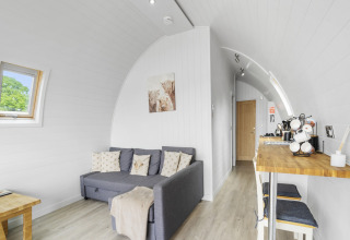 Licht en gezellig interieur van de Highland Camping Pod met bank, houten tafel en kitchenette in het Verenigd Koninkrijk.