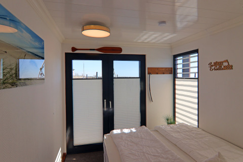 Bedroom on a houseboat featuring double doors, windows, nautical wooden decor, and white walls.