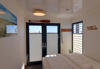 Dormitorio en una casa flotante con puertas dobles, ventanas, decoración náutica y paredes blancas.