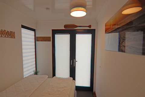 Houseboat bedroom with bed, double glass doors, wall art and ceiling light in Family & Friends in Germany.