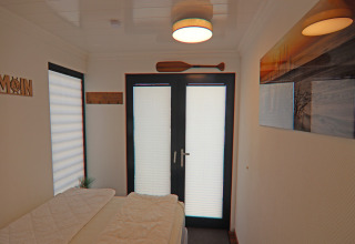 Houseboat bedroom with bed, double glass doors, wall art and ceiling light in Family & Friends in Germany.