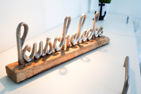 Metal sculpture spelling 'kuschelecke' on wooden base, displayed on a white surface in a houseboat.