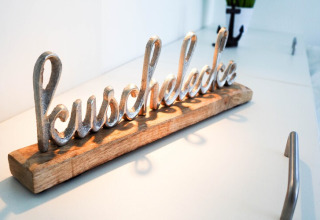 Metal sculpture spelling 'kuschelecke' on wooden base, displayed on a white surface in a houseboat.