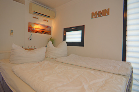 Bright and cozy bedroom on a houseboat with a double bed, wall decorations, and a small window.